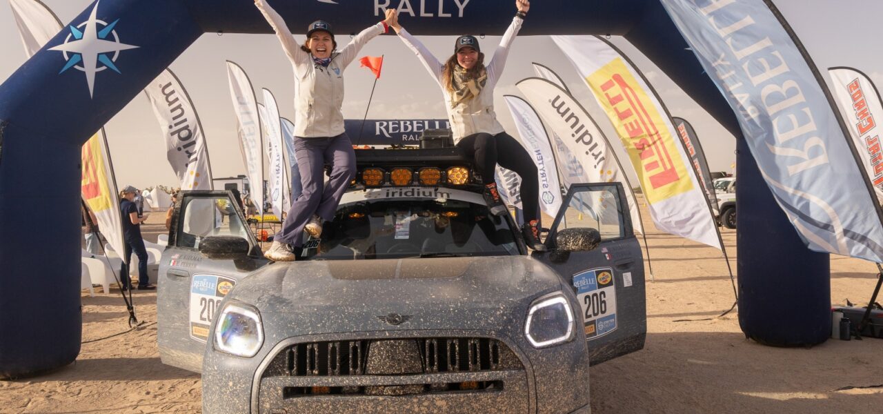 L’équipage MINI debout sur le capot du Countryman Untamed Edition, bras levés, sous l’arche d’arrivée de la Rebelle Rally